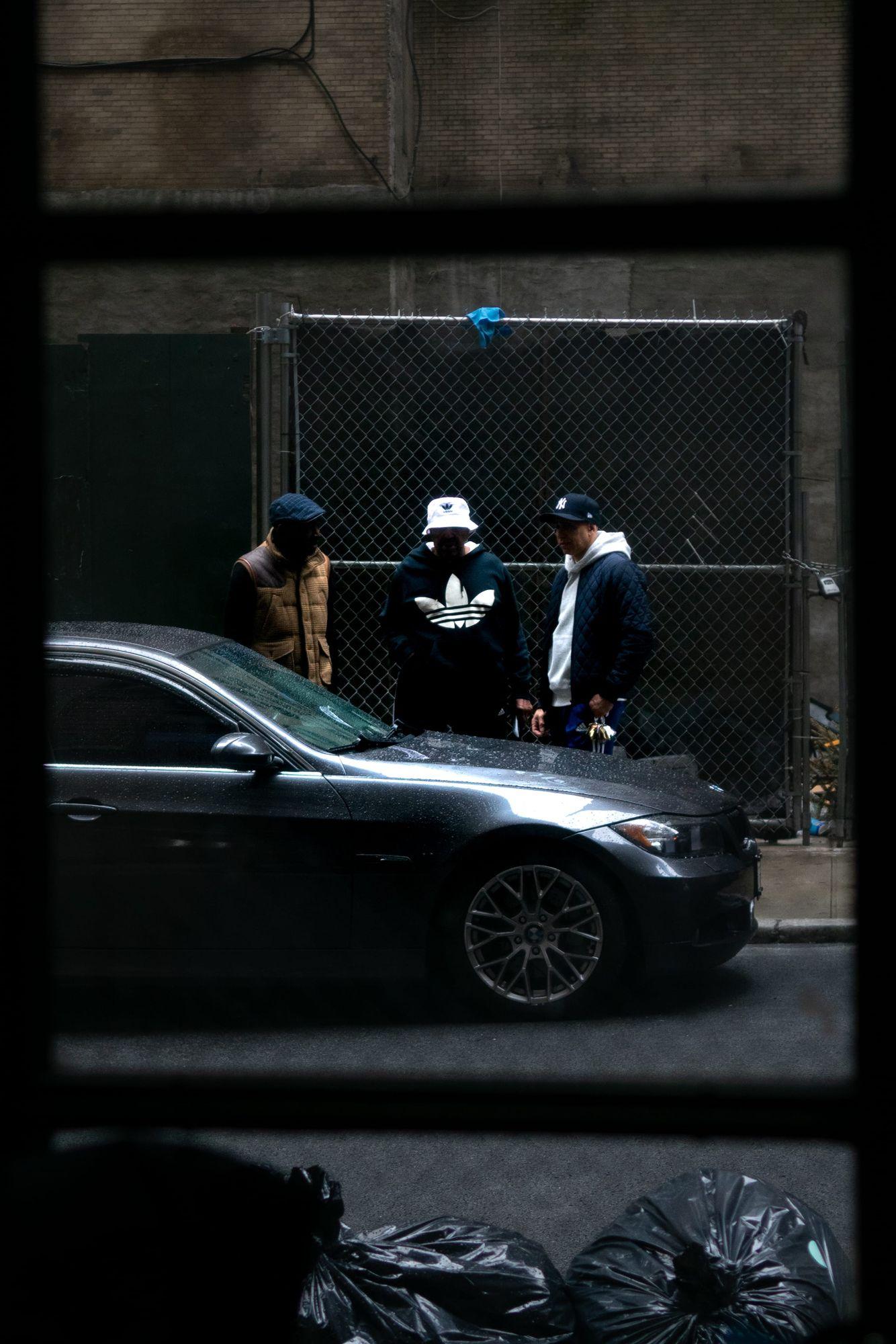 Three men talking behind a BMW, NYC